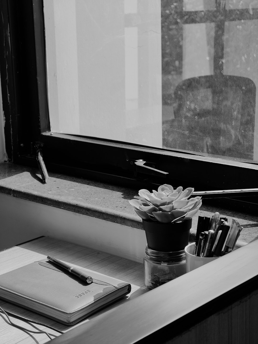 Minimalistischer Schreibtisch mit Notizbuch und Sukkulente an einem sonnigen Fenster.